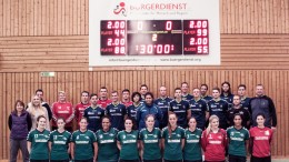Die Spielerinnen und Spieler der TuS 05 Daun Handballabteilung vor der durch den Bürgerdienst gesponserten Anzeigetagel in der Dauner Wehrbüschturnhalle
